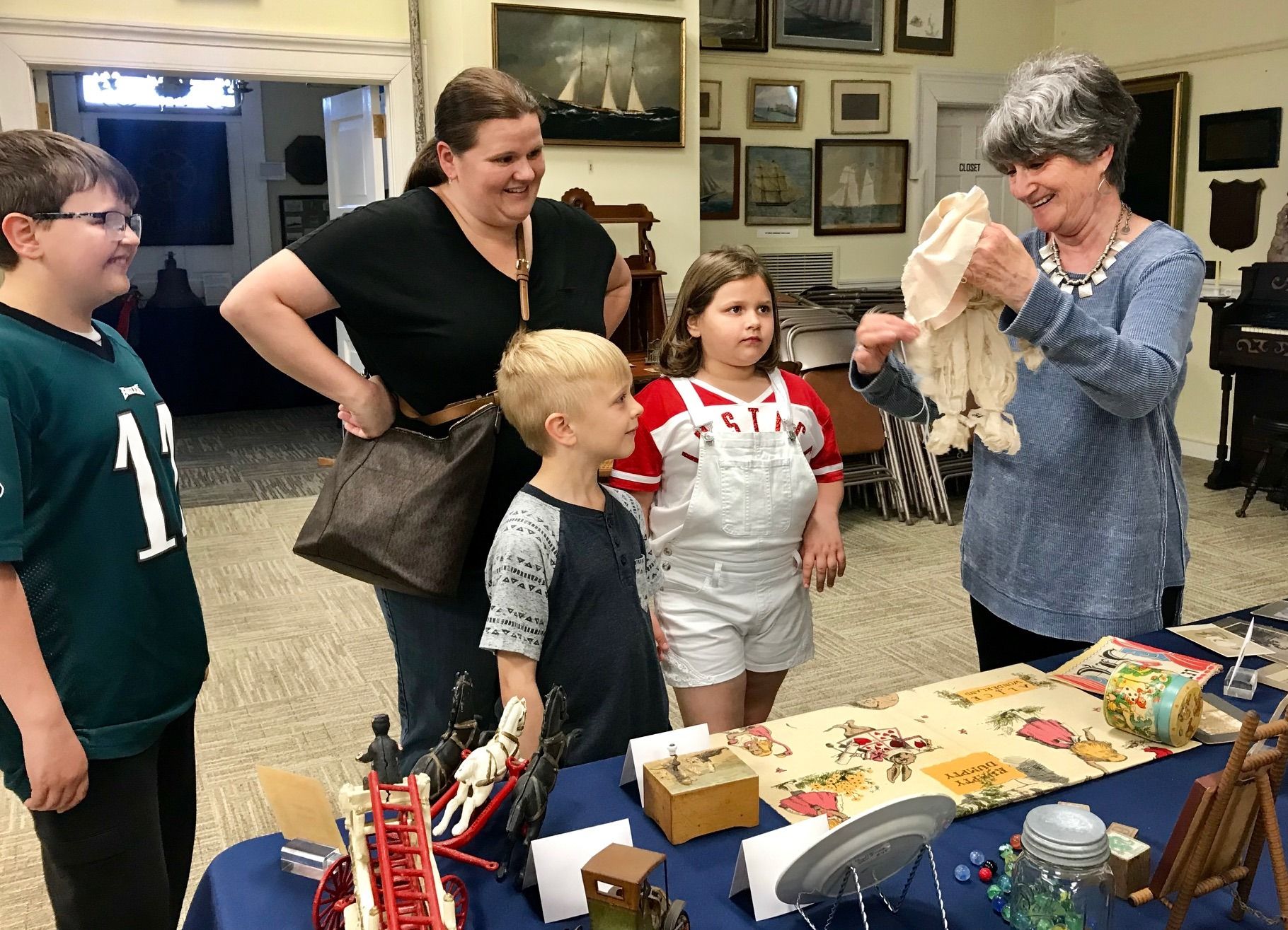 Woman and three children looking at antique dollclothes, held by museum curator