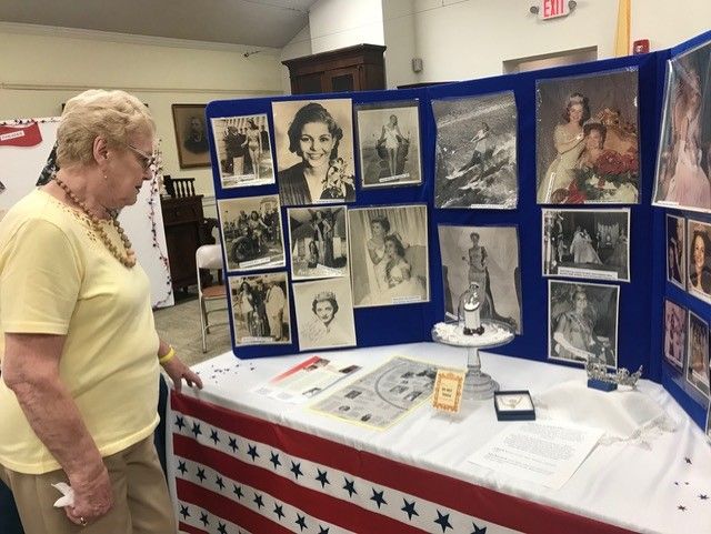 woman standing at table viewing a board with photographs mounted on it. Table has other photographs and artifacts, all of Miss America.
